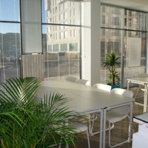Spacious, sunlit office lounge featuring white tables and chairs with a modern aesthetic.