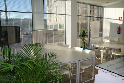 Spacious, sunlit office lounge featuring white tables and chairs with a modern aesthetic.