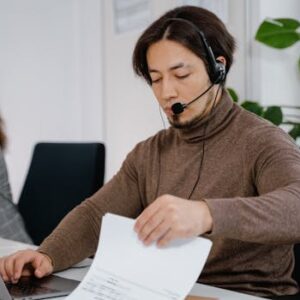 Man in headset working at a desk with laptop and papers in a modern office.