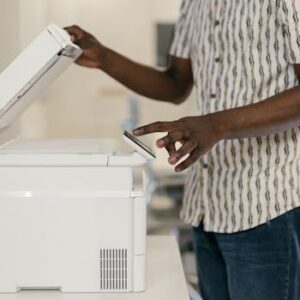 Person operating photocopier in modern office setting, engaging with technology.